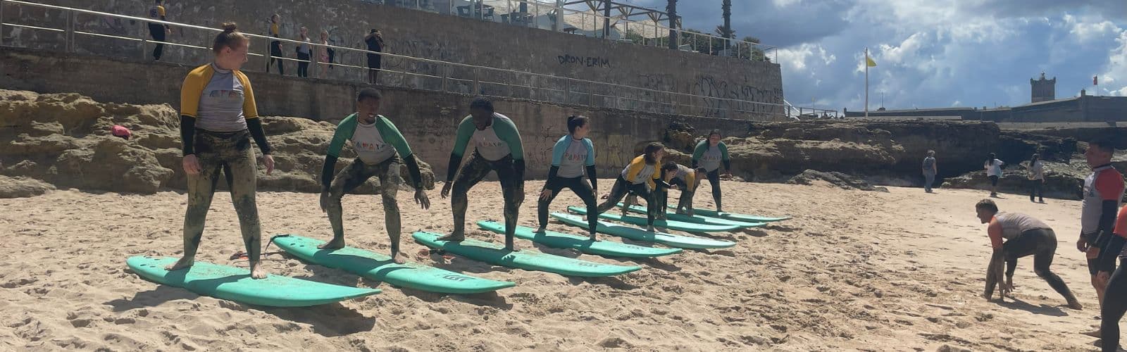 Six students stand on teal surfboards on the stand and practice movements. 